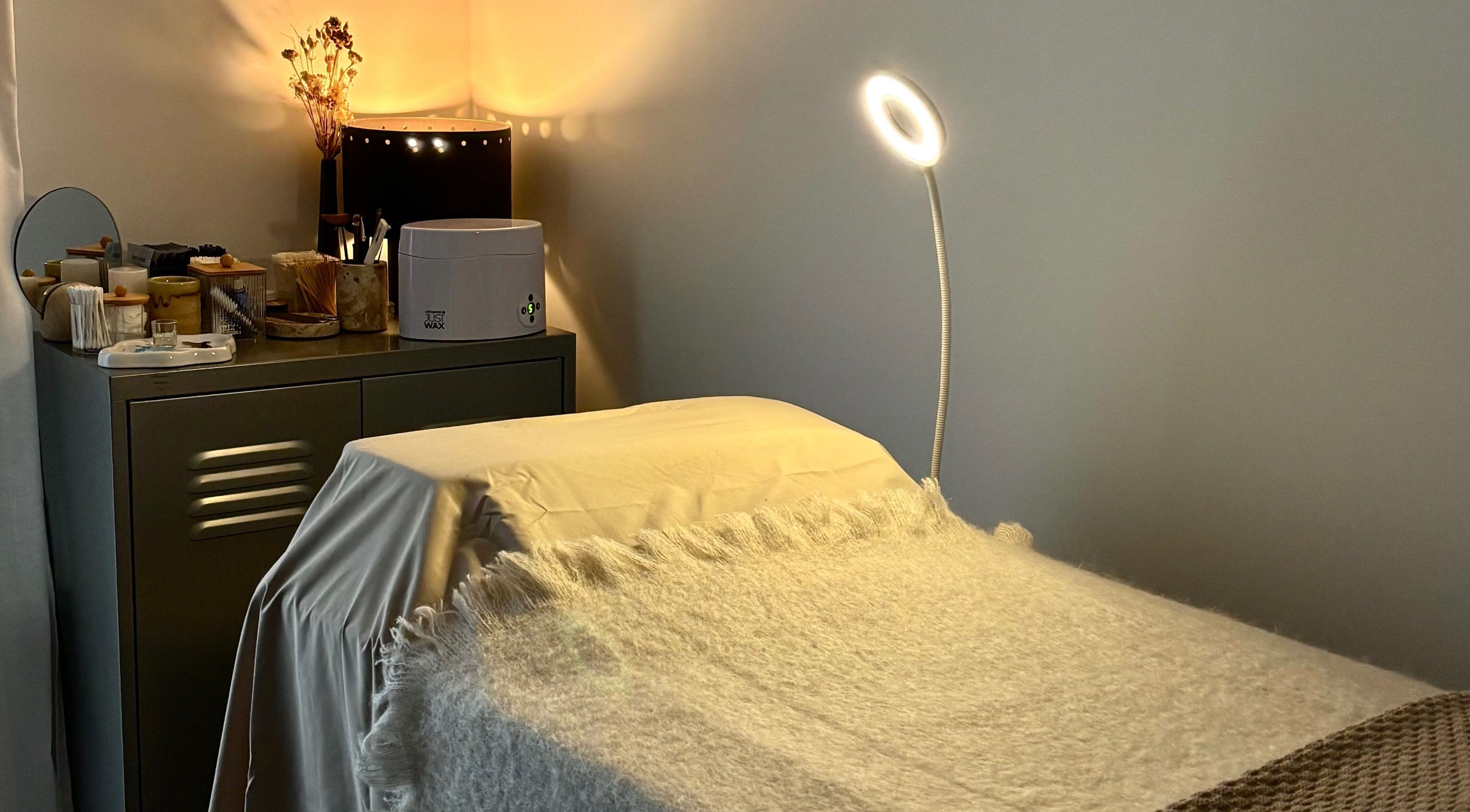 Cozy treatment bed in LAÙ Treatment Studio, Loughton, England, GB, with warm lighting and beauty products.