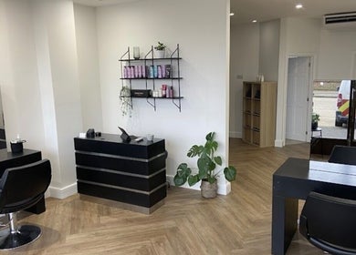 Spacious, modern interior of Libby’s Hair, Worthing, England, GB, featuring sleek black furniture and plant decor.