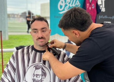 Coiffure chez Chez Dam’s, Garidech, Occitanie, FR, un barbier stylise la barbe d'un client.