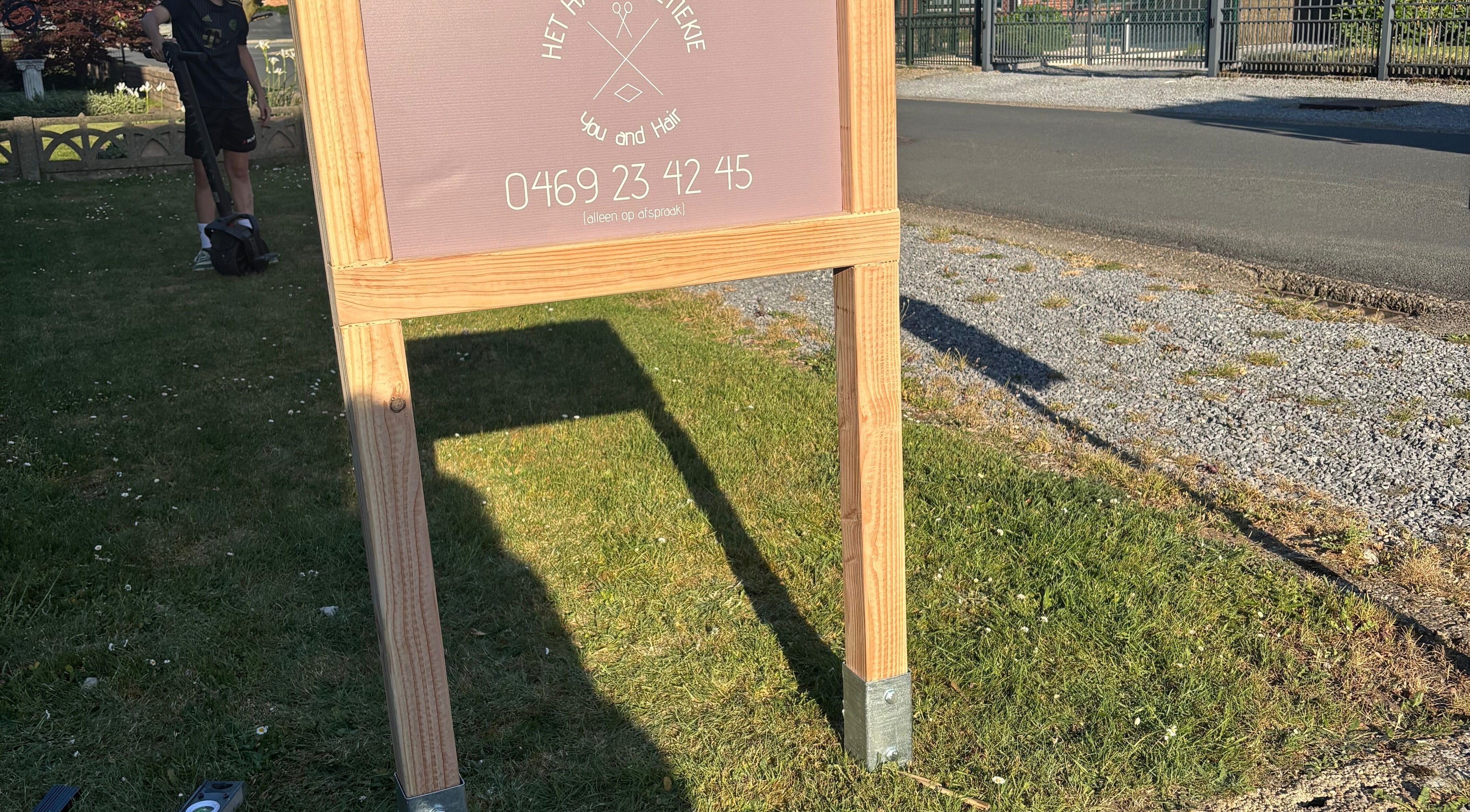 Bord van HethaarBoetiekje op grasveld bij Maaseik, Vlaanderen, BE met telefoonnummer vermeld.