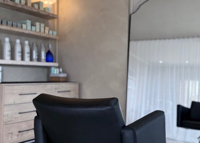 Stylish black salon chair at Tam’s Chair, Cape Town, Western Cape, ZA with shelves of hair products.