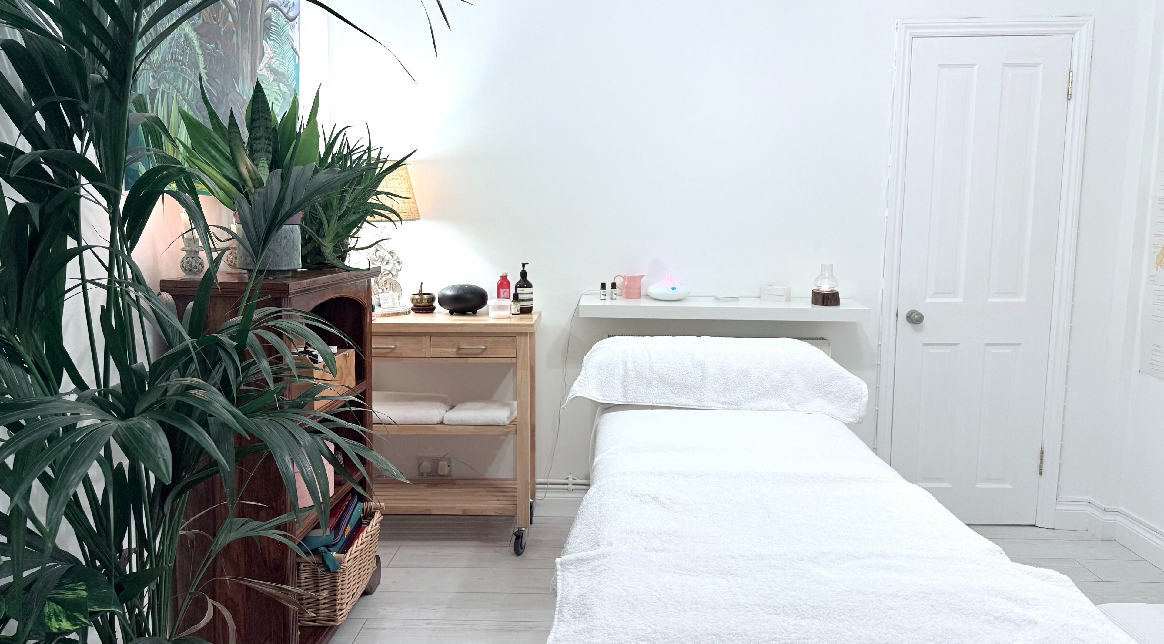Tranquil massage room at Gem Massage Therapy, Enfield, England, GB with lush plants and a cozy treatment bed.