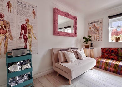 Gem Massage Therapy, Enfield, England, GB features a cozy room with anatomy posters, sofas, and vibrant decor.