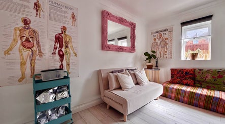 Gem Massage Therapy, Enfield, England, GB features a cozy room with anatomy posters, sofas, and vibrant decor.