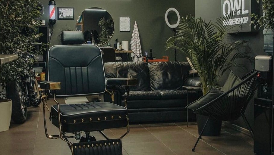 Elegant interior of OWL Barbershop in Rīga, LV, featuring comfy seating and lush greenery.