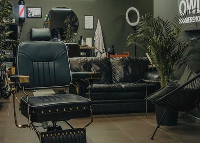 Elegant interior of OWL Barbershop in Rīga, LV, featuring comfy seating and lush greenery.
