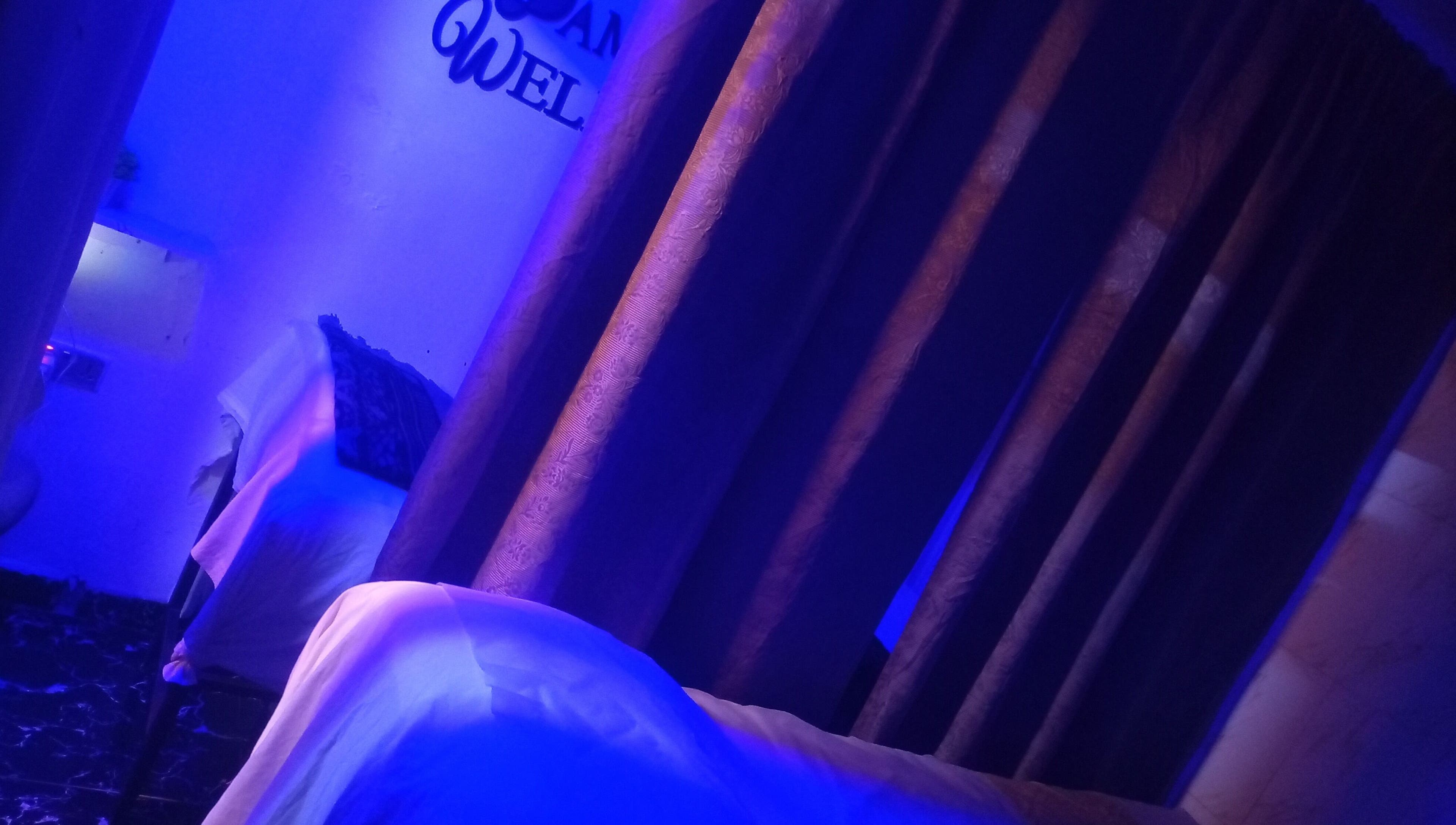 Tranquil massage room at Damme's Wellness in Lagos, Lagos, NG featuring soothing blue lighting and curtains.