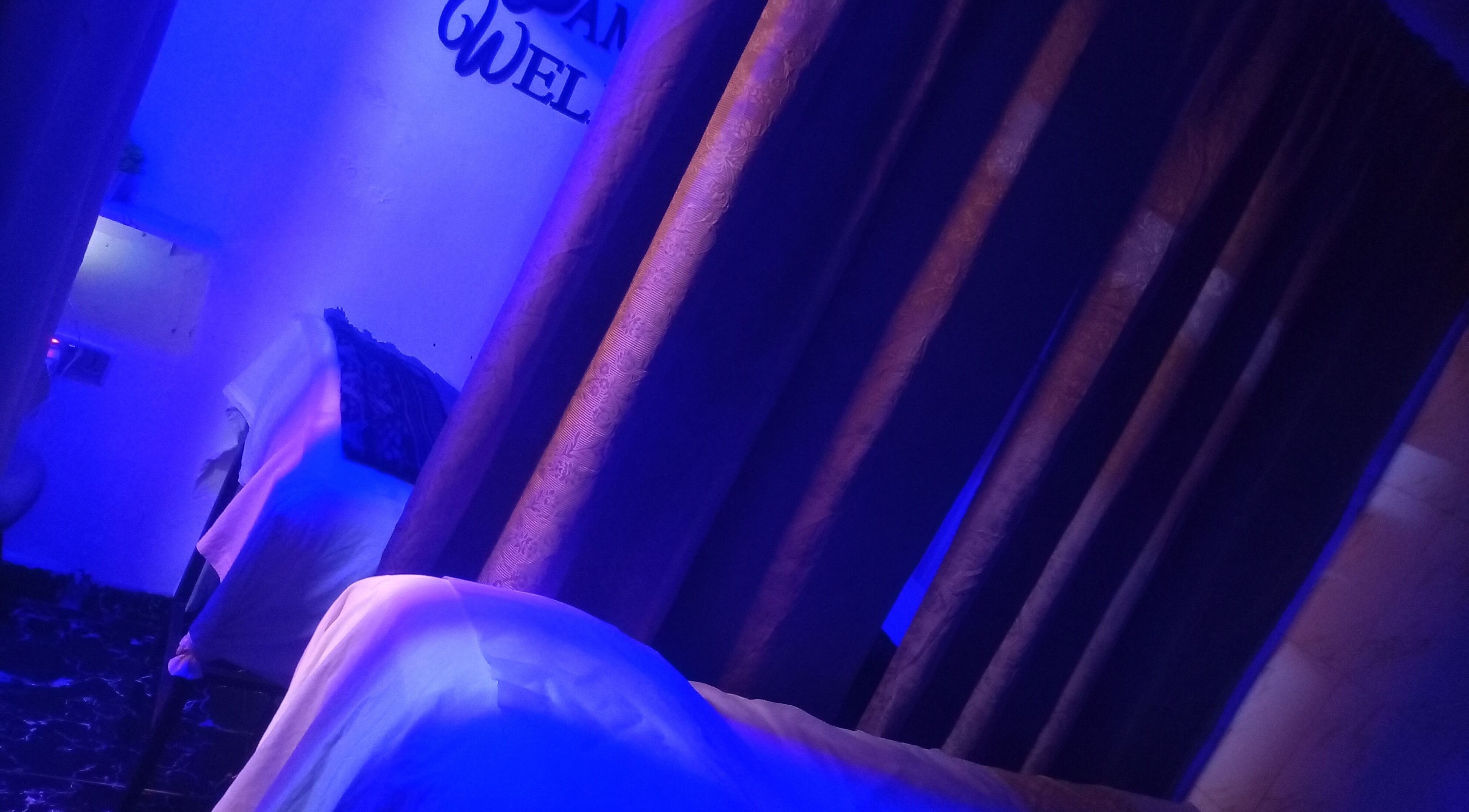 Tranquil massage room at Damme's Wellness in Lagos, Lagos, NG featuring soothing blue lighting and curtains.