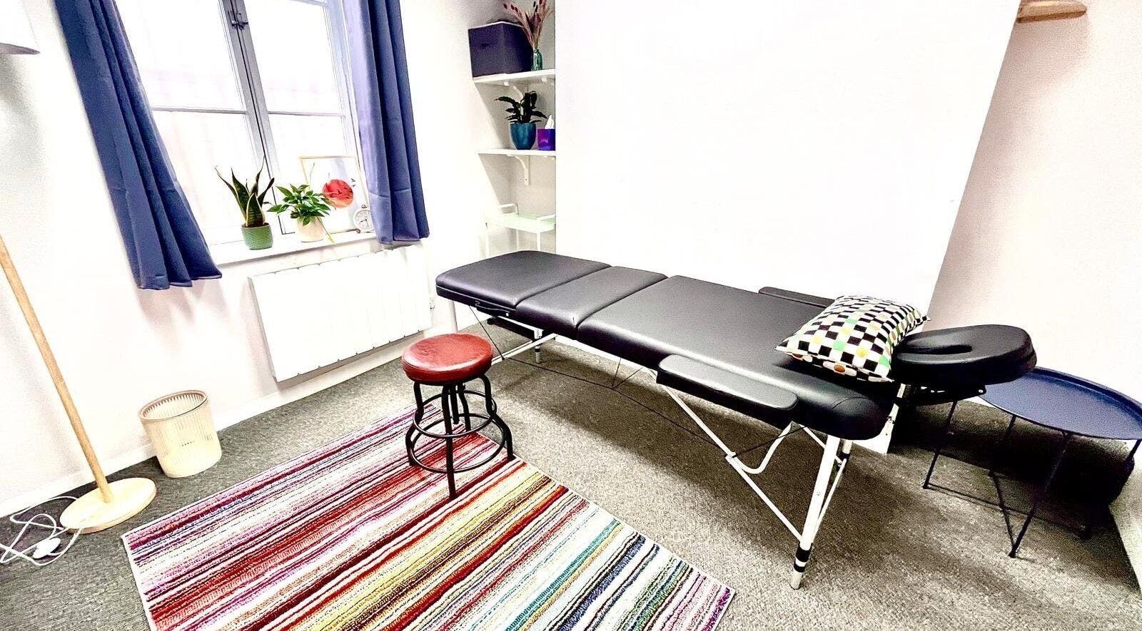 Massage table at Palms of Health, London, England, GB, in bright room with colorful rug and plants.
