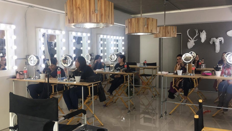 Interior del Sara Maldonado Makeup Studio en Guadalupe, Nuevo León, MX, con tocadores iluminados y clientes aplicándose maquillaje.