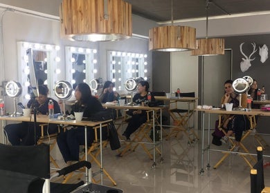 Interior del Sara Maldonado Makeup Studio en Guadalupe, Nuevo León, MX, con tocadores iluminados y clientes aplicándose maquillaje.