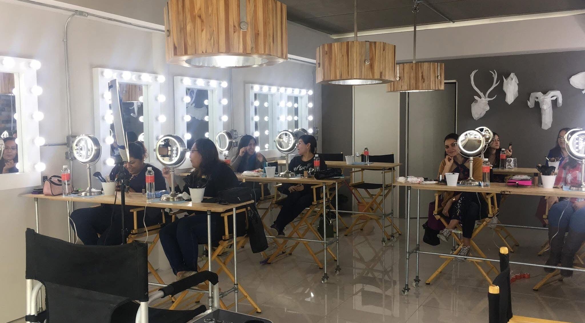 Interior del Sara Maldonado Makeup Studio en Guadalupe, Nuevo León, MX, con tocadores iluminados y clientes aplicándose maquillaje.