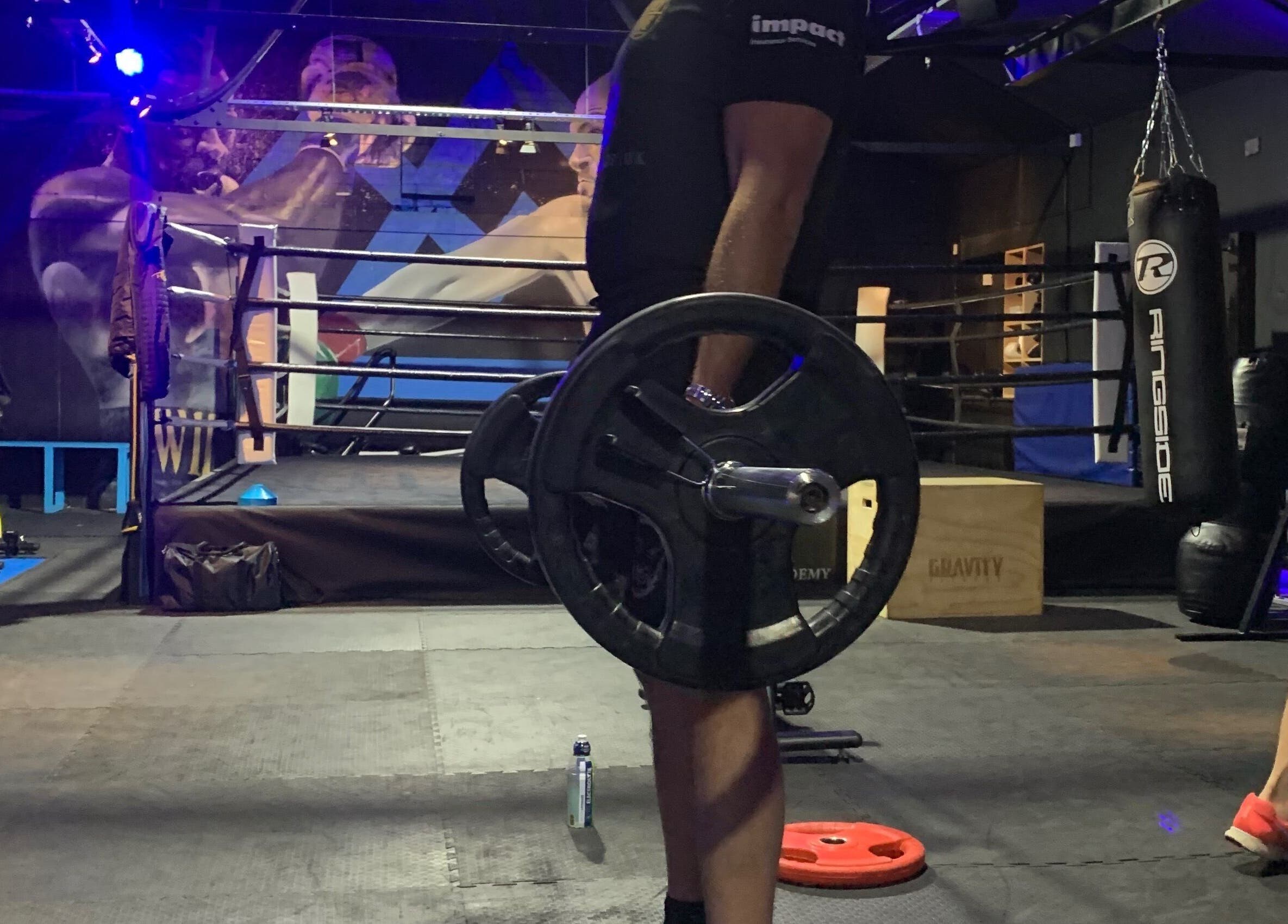 Weightlifting session at Conquer Boxing & Fitness in Ormskirk, England. A man lifts a barbell in a dim-lit gym.