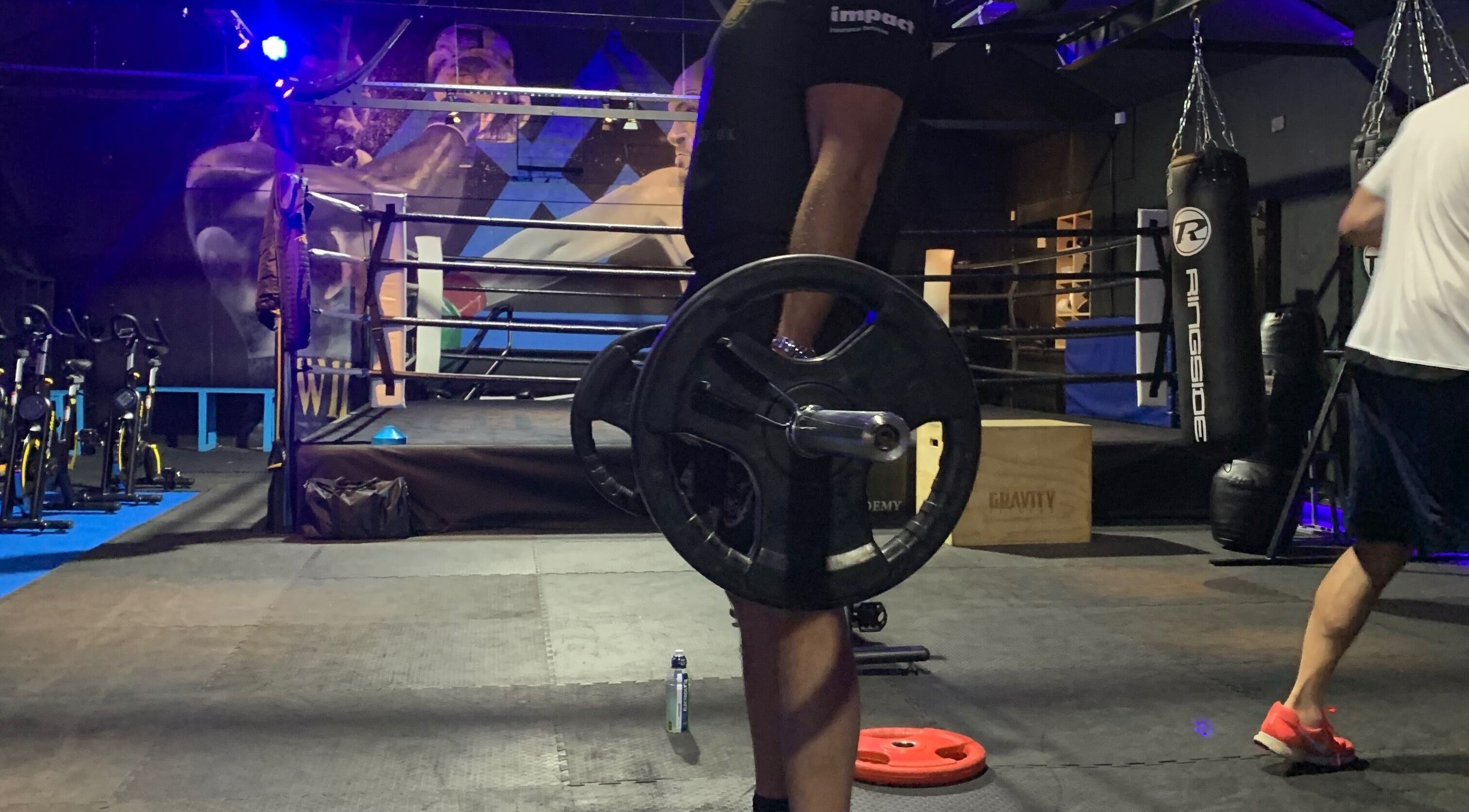 Weightlifting session at Conquer Boxing & Fitness in Ormskirk, England. A man lifts a barbell in a dim-lit gym.