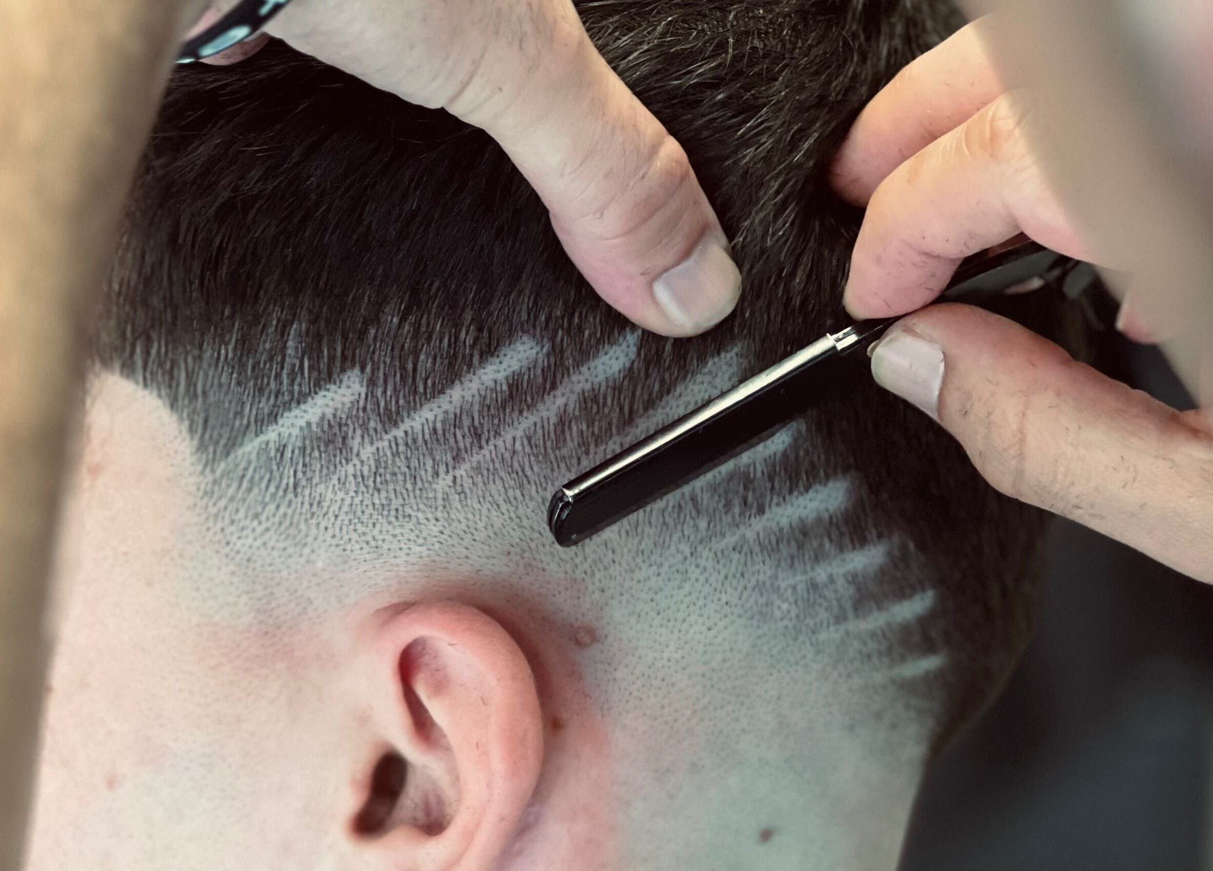 Barbeiro em Barbearia Alfa, Ovar, PT, realiza corte preciso com lâmina em design moderno.