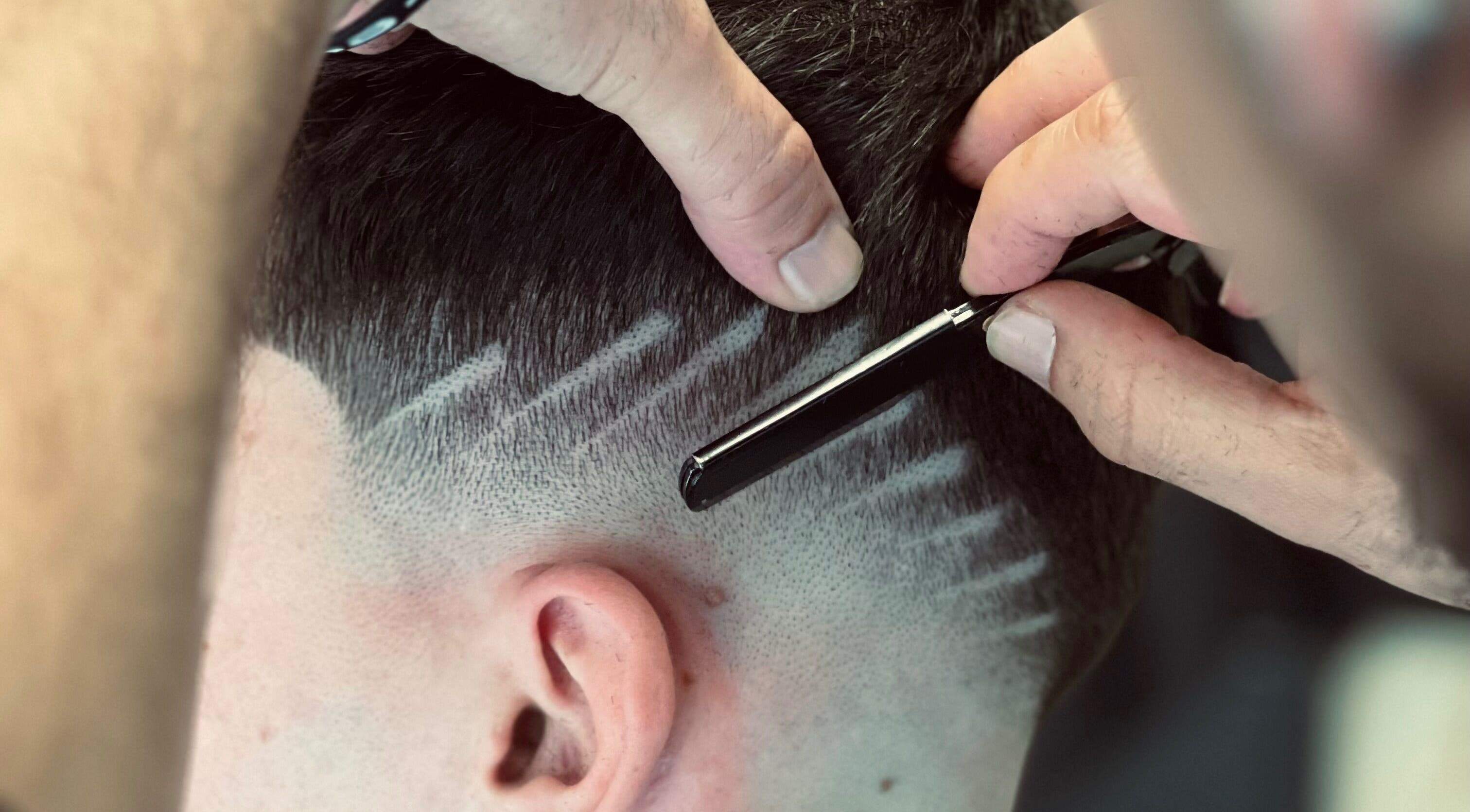 Barbeiro em Barbearia Alfa, Ovar, PT, realiza corte preciso com lâmina em design moderno.