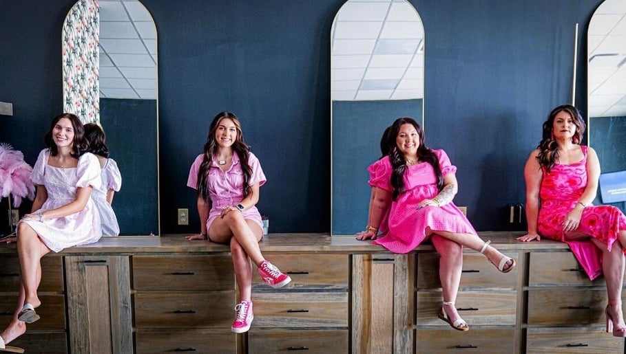 Four women in vibrant dresses at SG Stylez Hair Salon, Wills Point, Texas, US, seated by tall mirrors.
