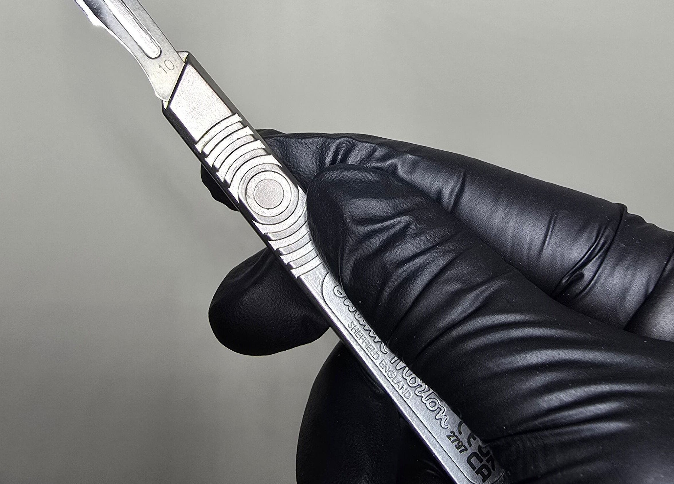 Close-up of a scalpel held in gloved hand at Glam Studio, Cape Town, Western Cape, ZA.