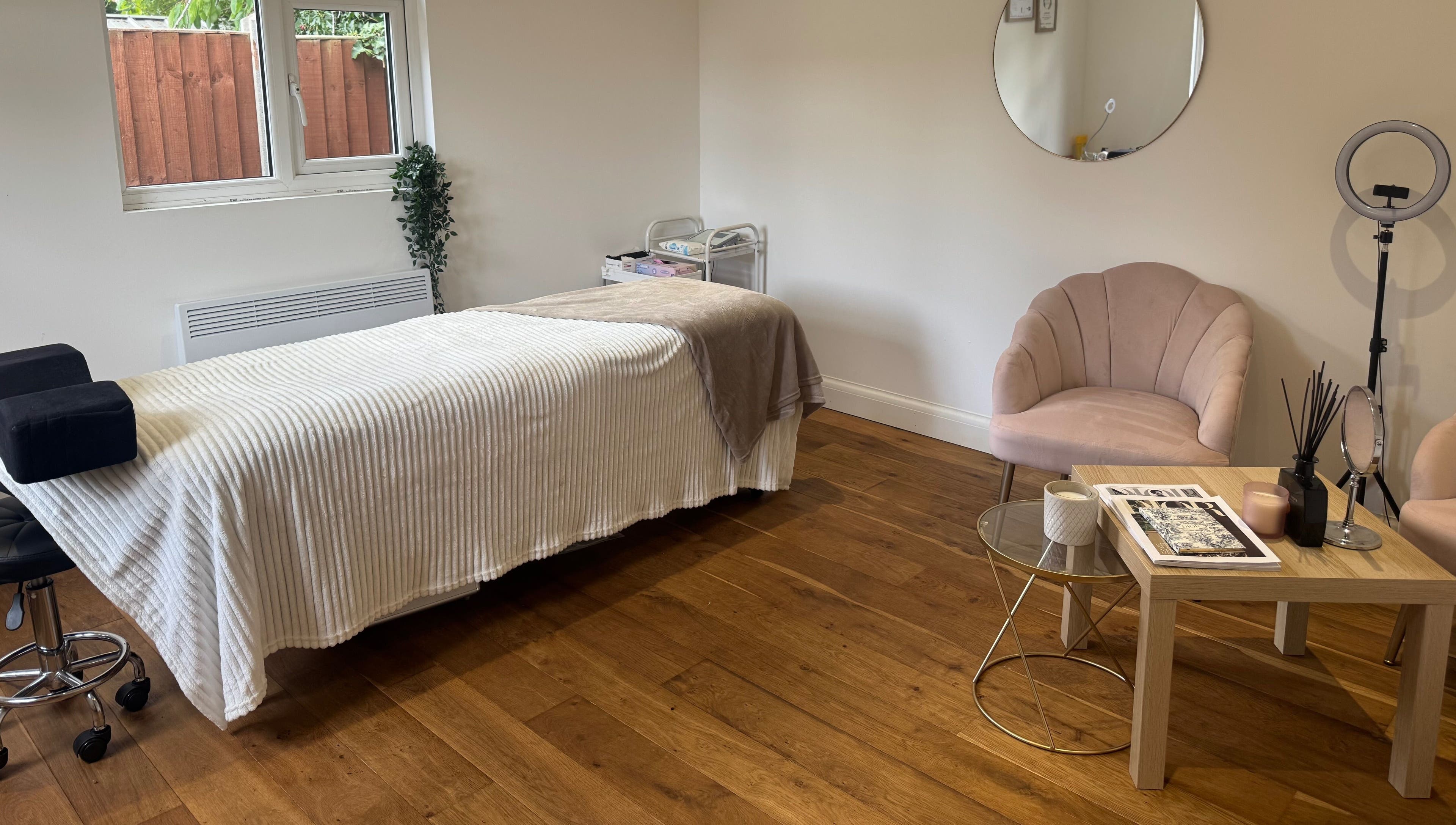 Calm treatment room at Arch & Lash co. in Guildford, England, featuring a massage bed and cozy seating.