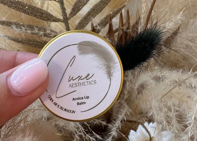 Hand holding Luxe Aesthetics By Meg Arnica Lip Balm in Chepstow, Wales, GB surrounded by fluffy decor.