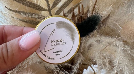 Hand holding Luxe Aesthetics By Meg Arnica Lip Balm in Chepstow, Wales, GB surrounded by fluffy decor.