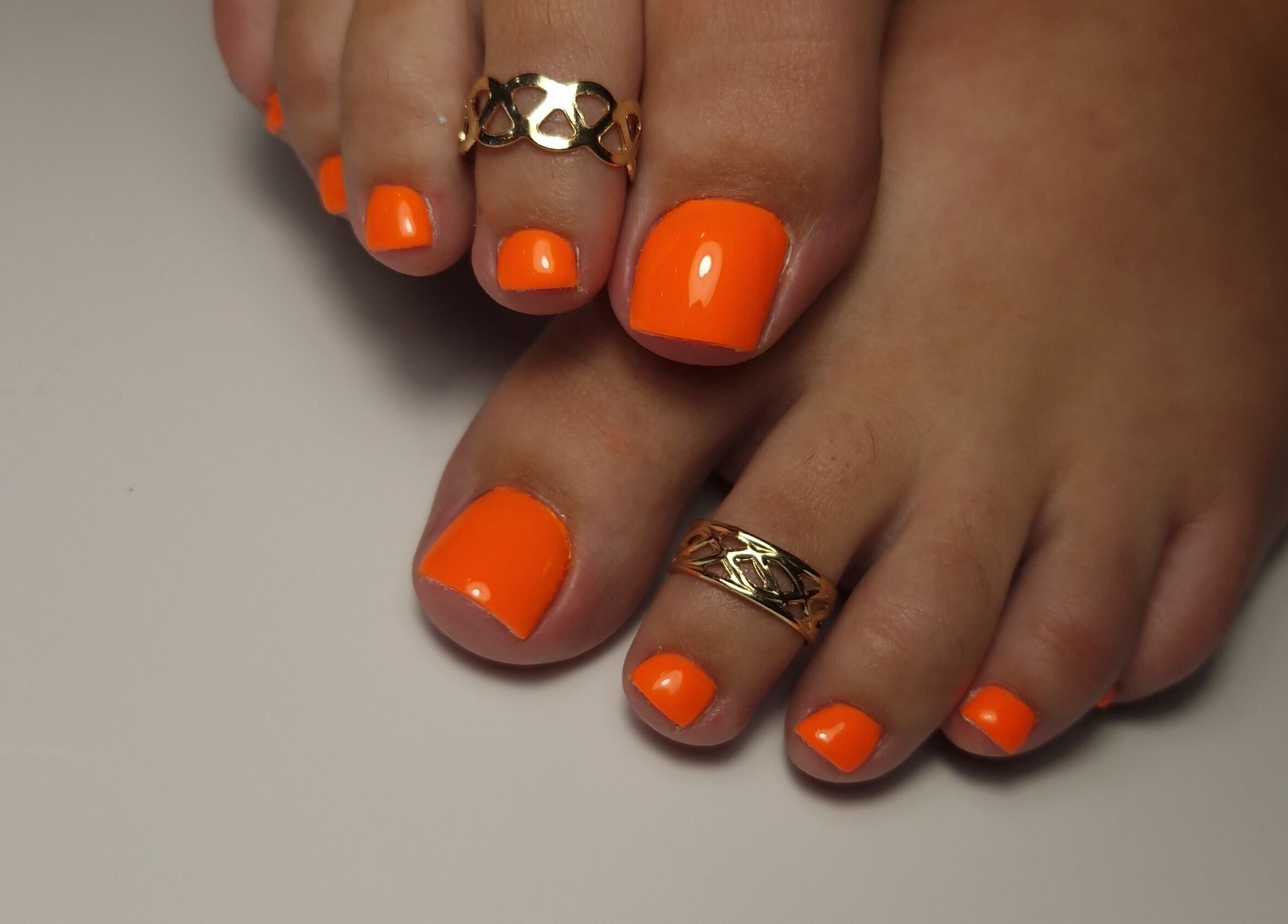 Pédicure orange vif avec bagues chez Melianails, Étoile-sur-Rhône, Auvergne-Rhône-Alpes, FR.