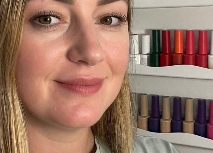 Technicienne souriante chez Ongles & Sourcils Mariia (Chez Studio Rebels), La Prairie, Québec, CA, devant vernis colorés.
