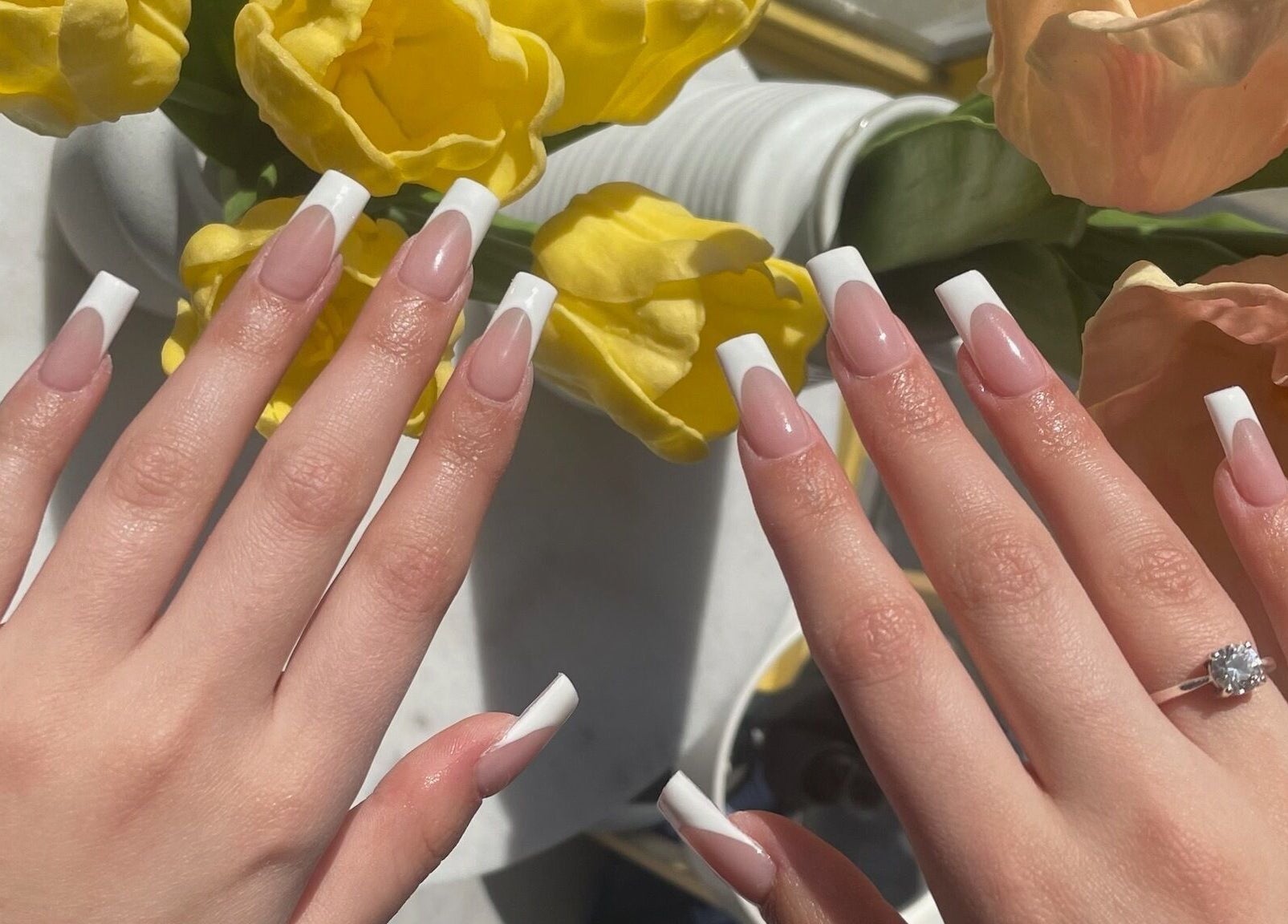 Elegant French manicure at Nail Haus, Toronto, Ontario, CA, with yellow tulips in the background.