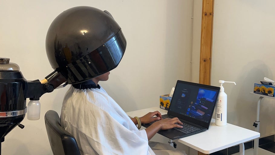 Client under hair dryer working on laptop at Braidsbyvuyo - Natural Hair Salon, Sandton, Gauteng, ZA.