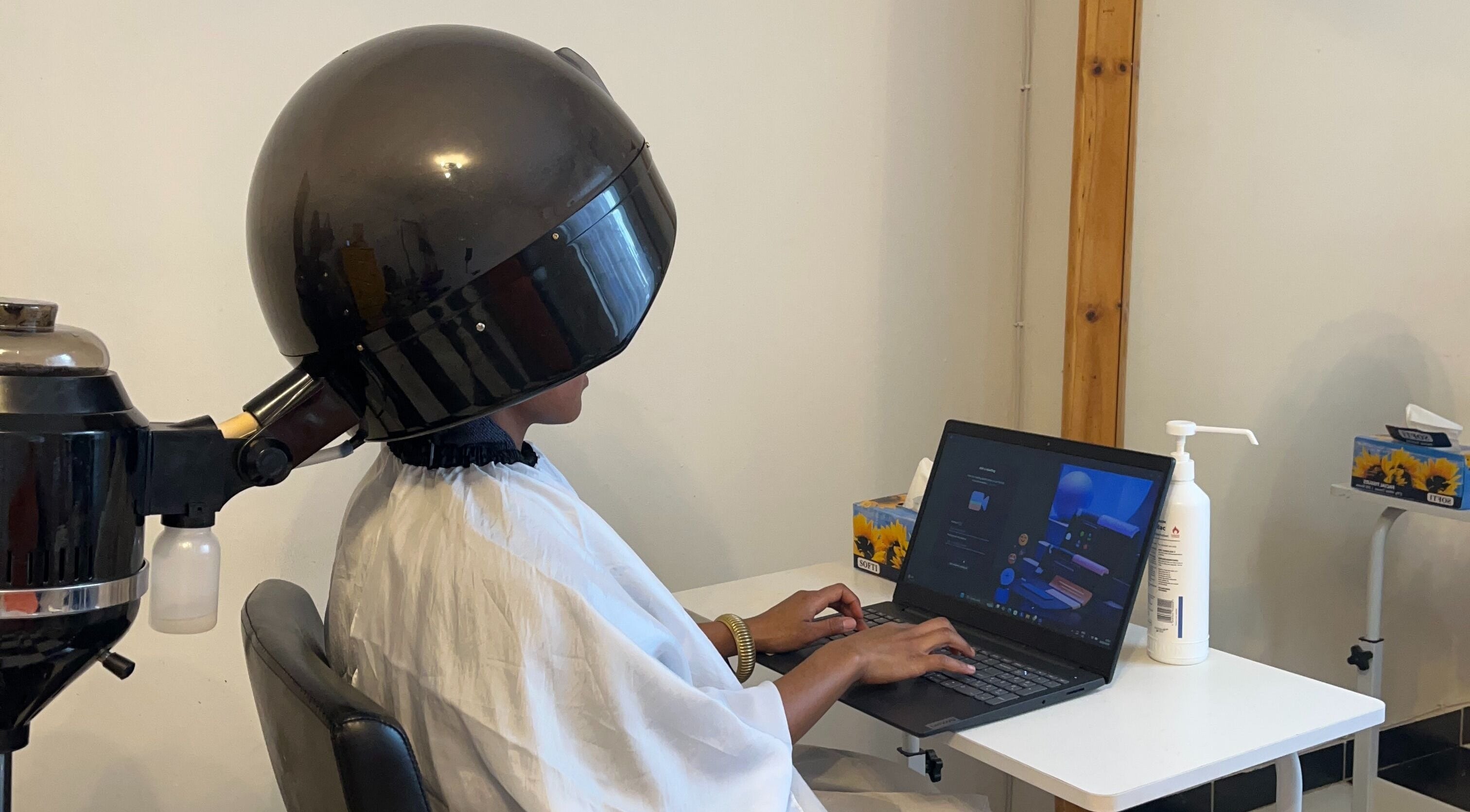 Client under hair dryer working on laptop at Braidsbyvuyo - Natural Hair Salon, Sandton, Gauteng, ZA.