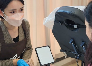 A specialist at AOh Beauty in Kowloon, HK, attentively consulting a client with a mirror in hand.