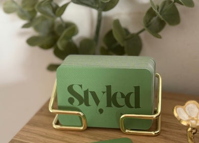 Green business cards with 'Styled by Jenna' logo in Blantyre, Scotland, GB displayed elegantly on a holder.