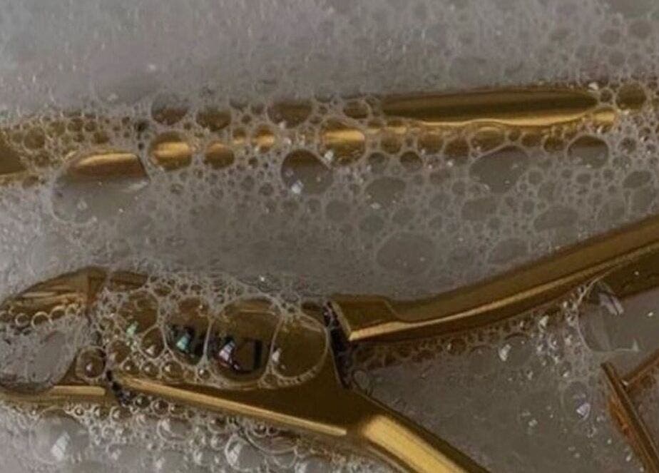 Golden grooming tools in soapy water at Classic Touch, Noord, AW, highlighting cleanliness and luxury.