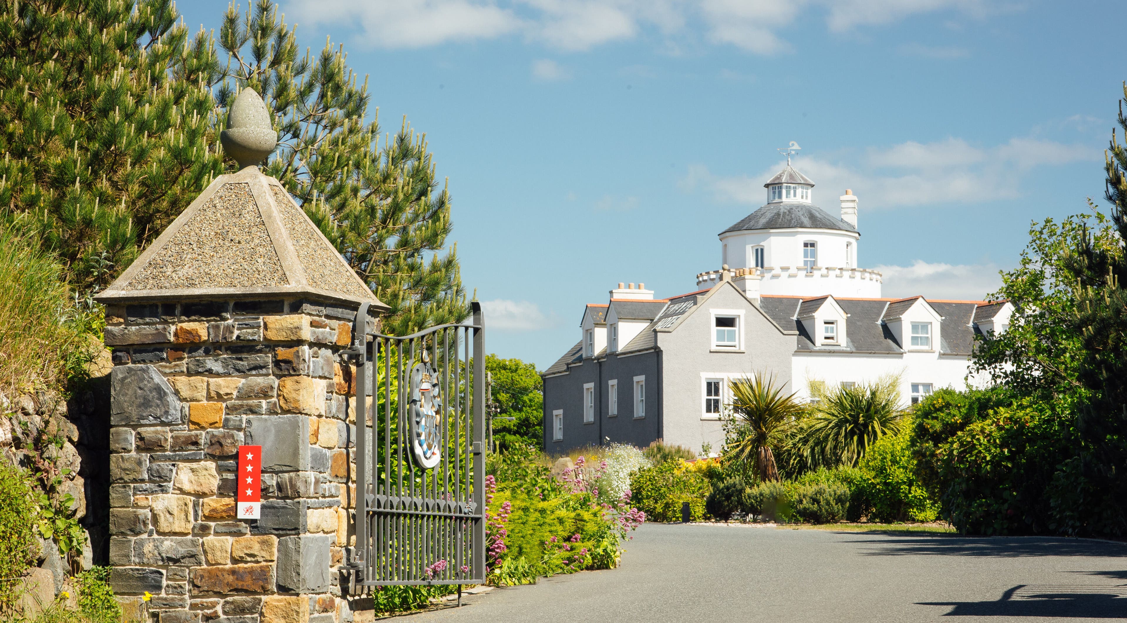 Elegant entrance of Twr y Felin Hotel in St Davids, Wales, GB, framed by lush greenery and blue skies.