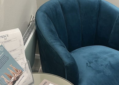 A plush blue chair beside brochures and price lists at The Clinic by Jessica May, Lowton, England, GB.
