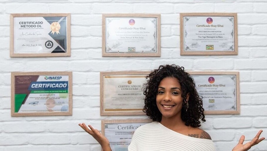 Profissional sorrindo com certificados na parede em Xantos Massagem, São Paulo, São Paulo, BR.