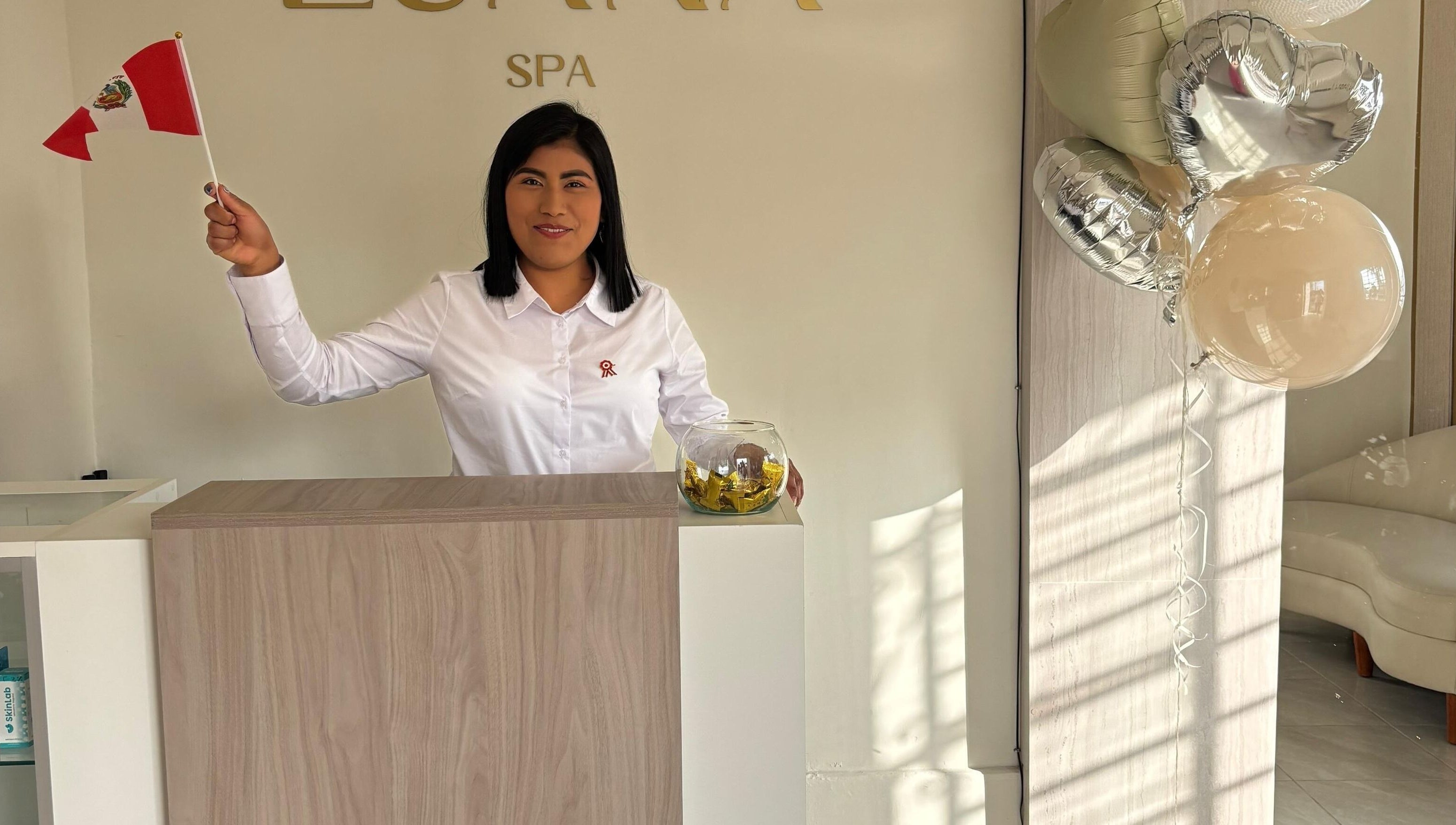 Receptionist at Luana Spa, Carmen De La Legua - Reynoso, Callao, PE, smiling with balloons and a small flag.