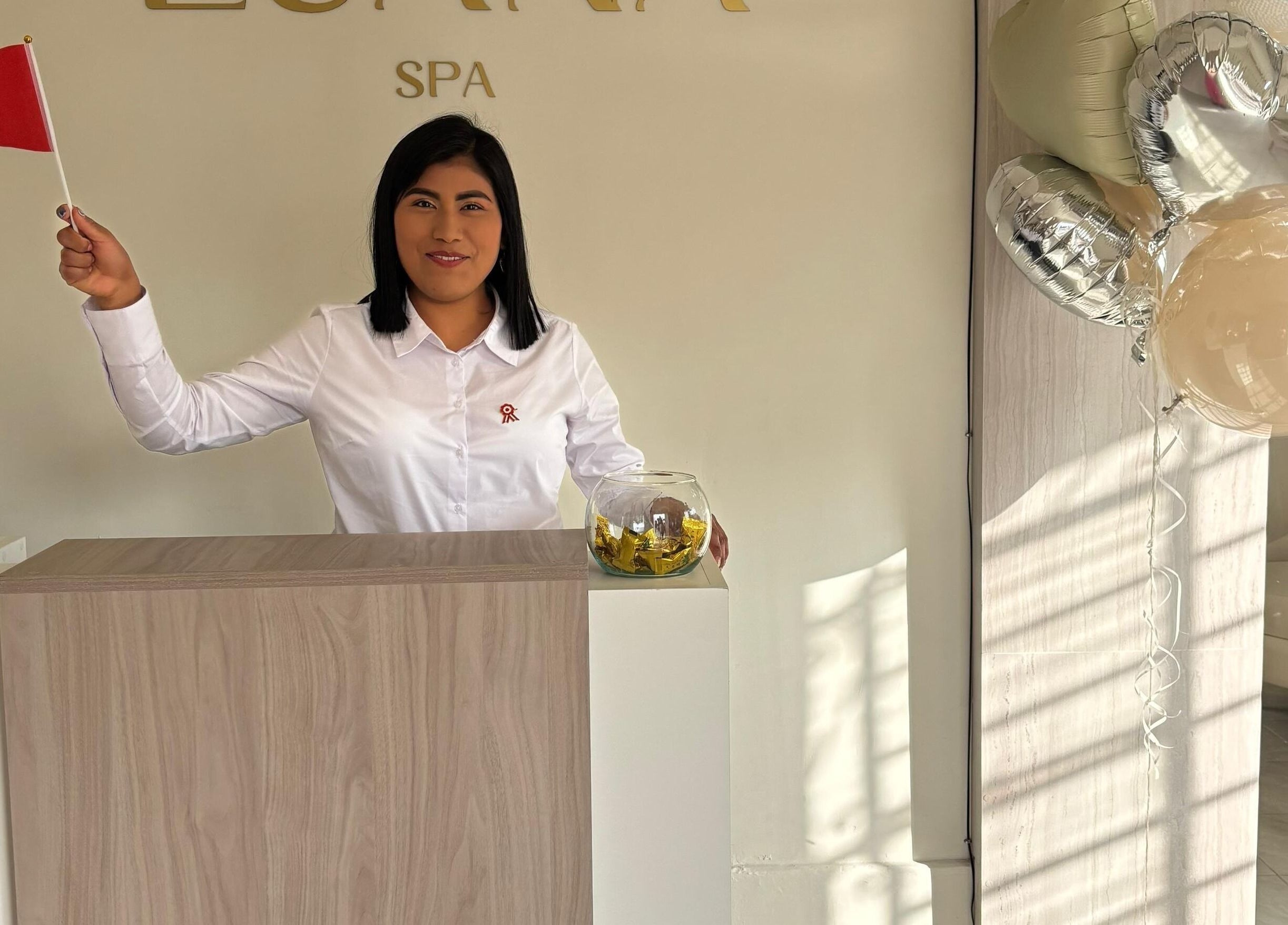 Receptionist at Luana Spa, Carmen De La Legua - Reynoso, Callao, PE, smiling with balloons and a small flag.