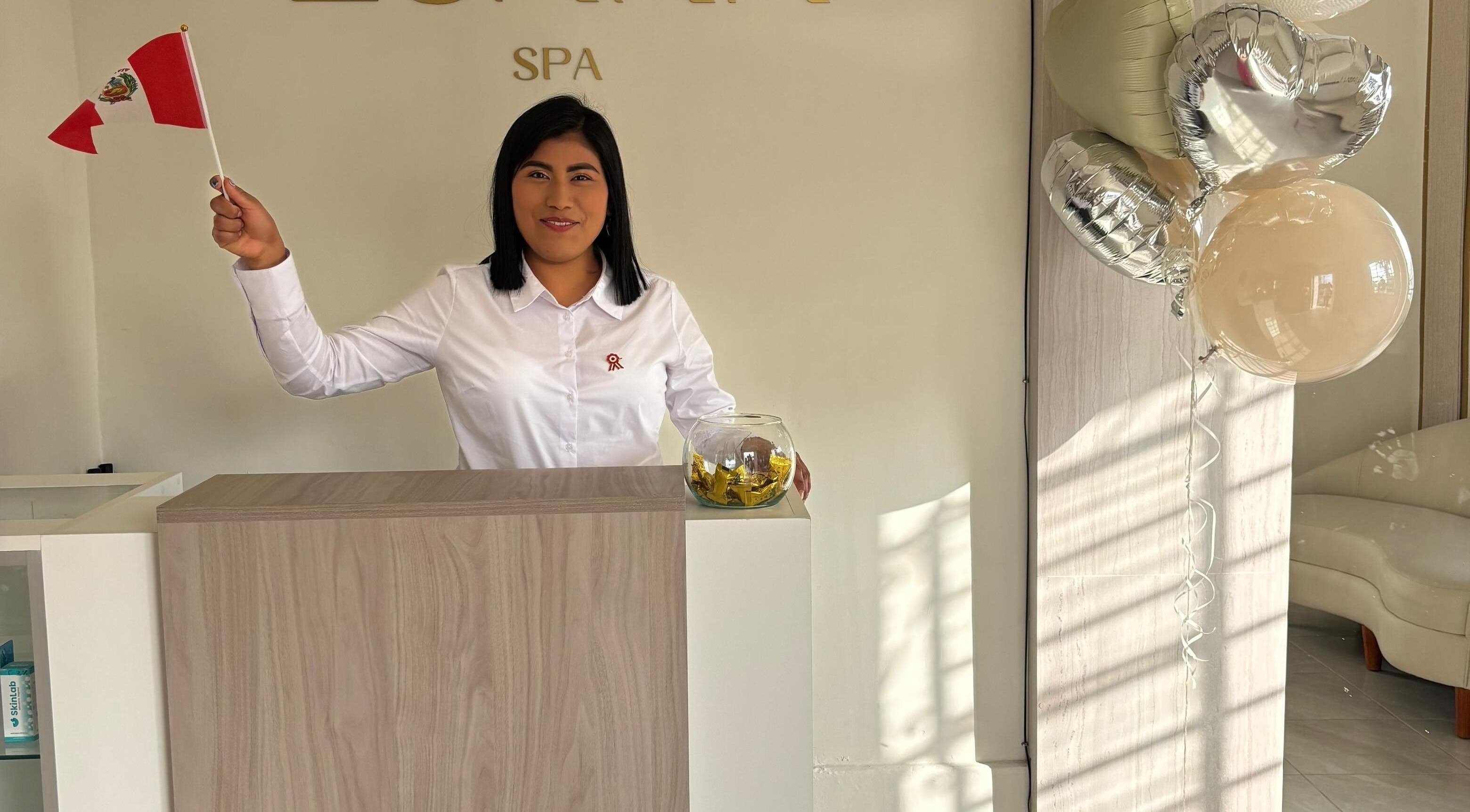 Receptionist at Luana Spa, Carmen De La Legua - Reynoso, Callao, PE, smiling with balloons and a small flag.