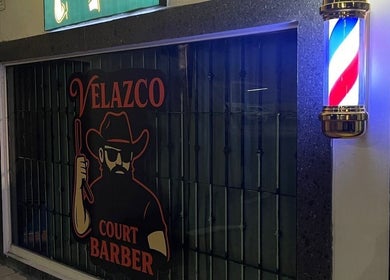 Fachada de Velazco Court Barber iluminada en Monterrey, Nuevo León, MX, con poste de barbero clásico.