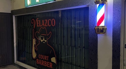 Fachada de Velazco Court Barber iluminada en Monterrey, Nuevo León, MX, con poste de barbero clásico.