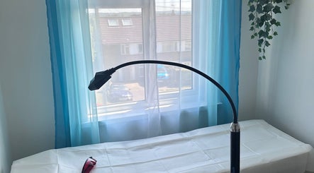 Bright treatment room at Pearl Bright, Reigate, England, GB, featuring a bed with blue curtains and a lamp.