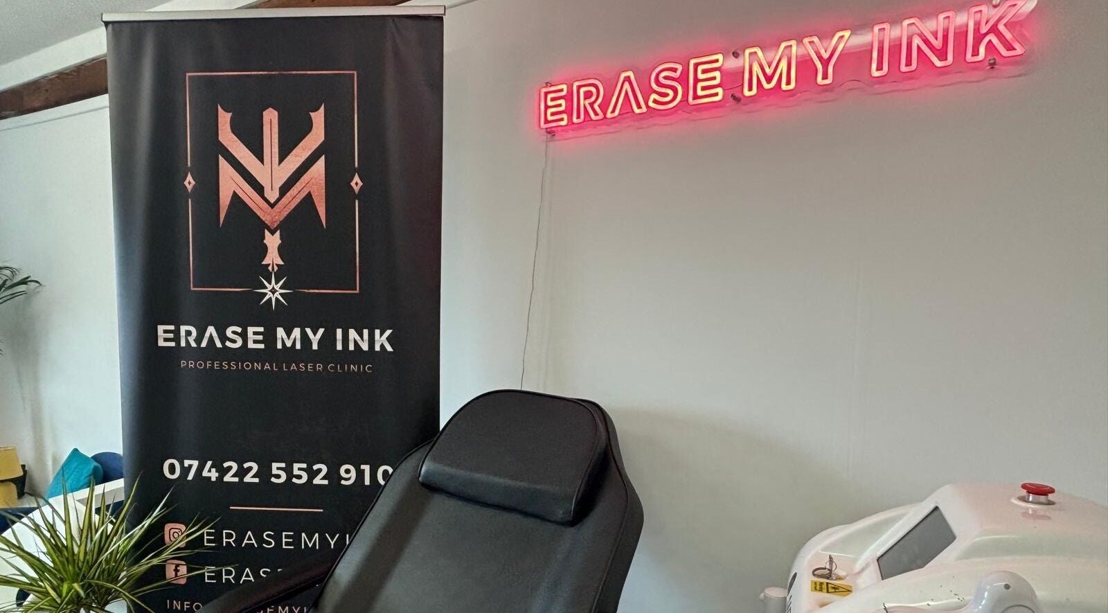 Erase My Ink clinic interior in Chelmsford, England featuring a modern treatment chair and neon signage.
