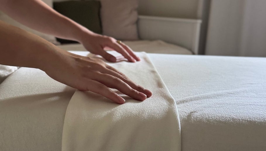 Hands smoothing a massage bed at Em-Bodywellness, Montréal, Québec, CA, showcasing a peaceful spa setting.