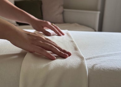 Hands smoothing a massage bed at Em-Bodywellness, Montréal, Québec, CA, showcasing a peaceful spa setting.