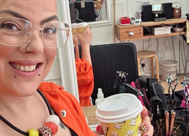 Smiling stylist with coffee at Ruth - Clippers Barber Shop, Daventry, England, GB.