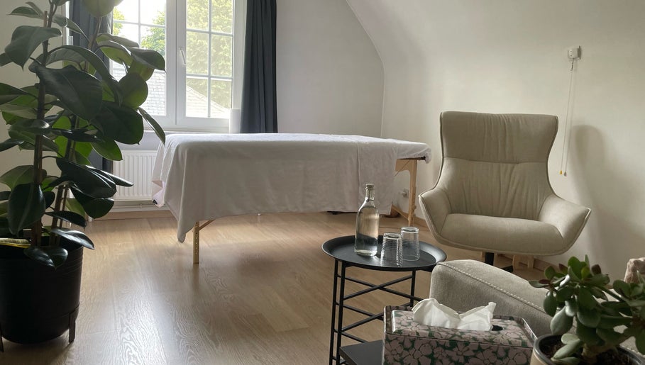 Rustige massagekamer bij De Waterlelie, Nazareth-de Pinte, Vlaanderen, BE met comfortabele stoel en plant.