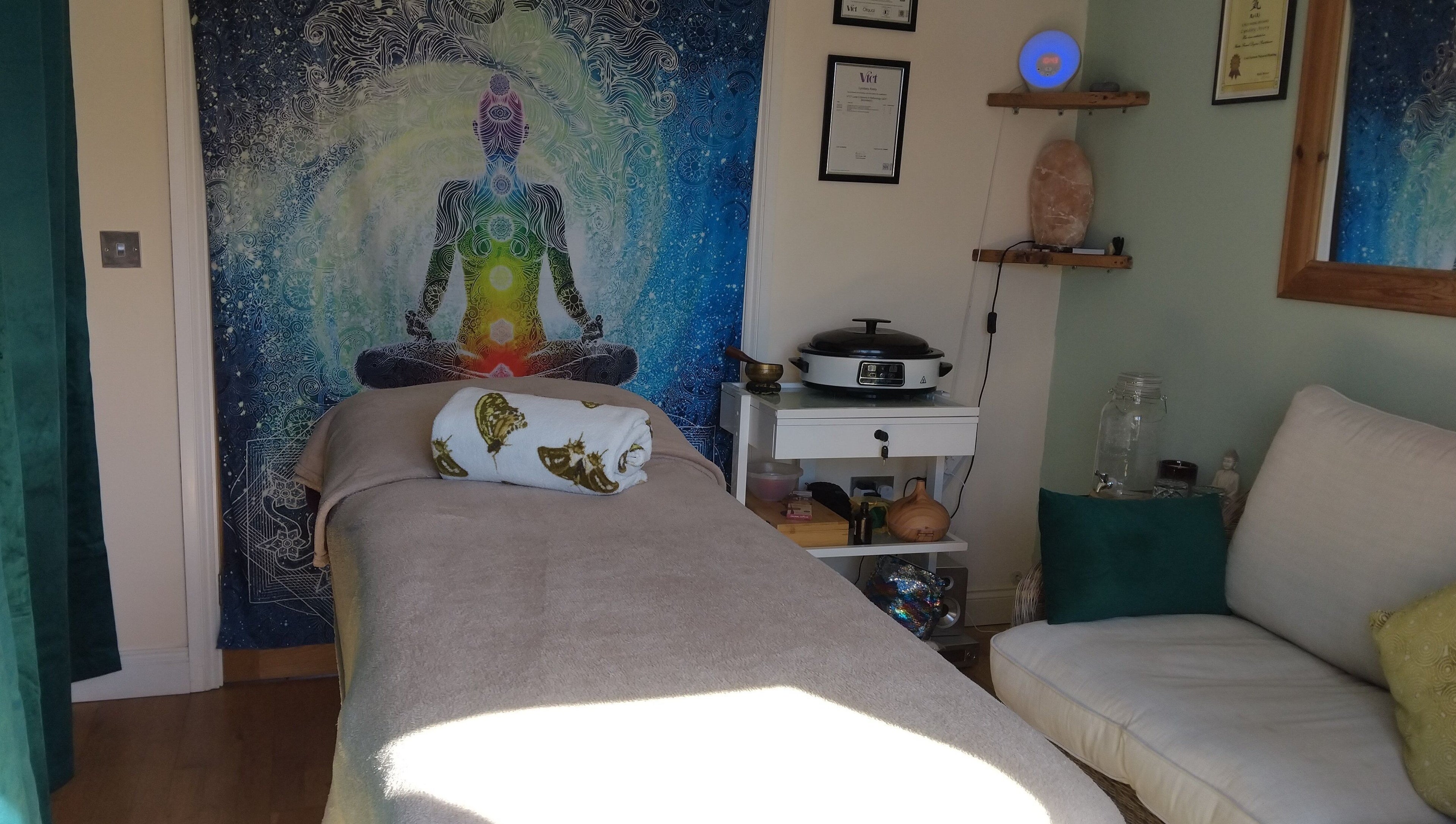 A serene therapy room at Bee Elevated Holistic Health in Holbury, England featuring a massage bed and chakra tapestry.