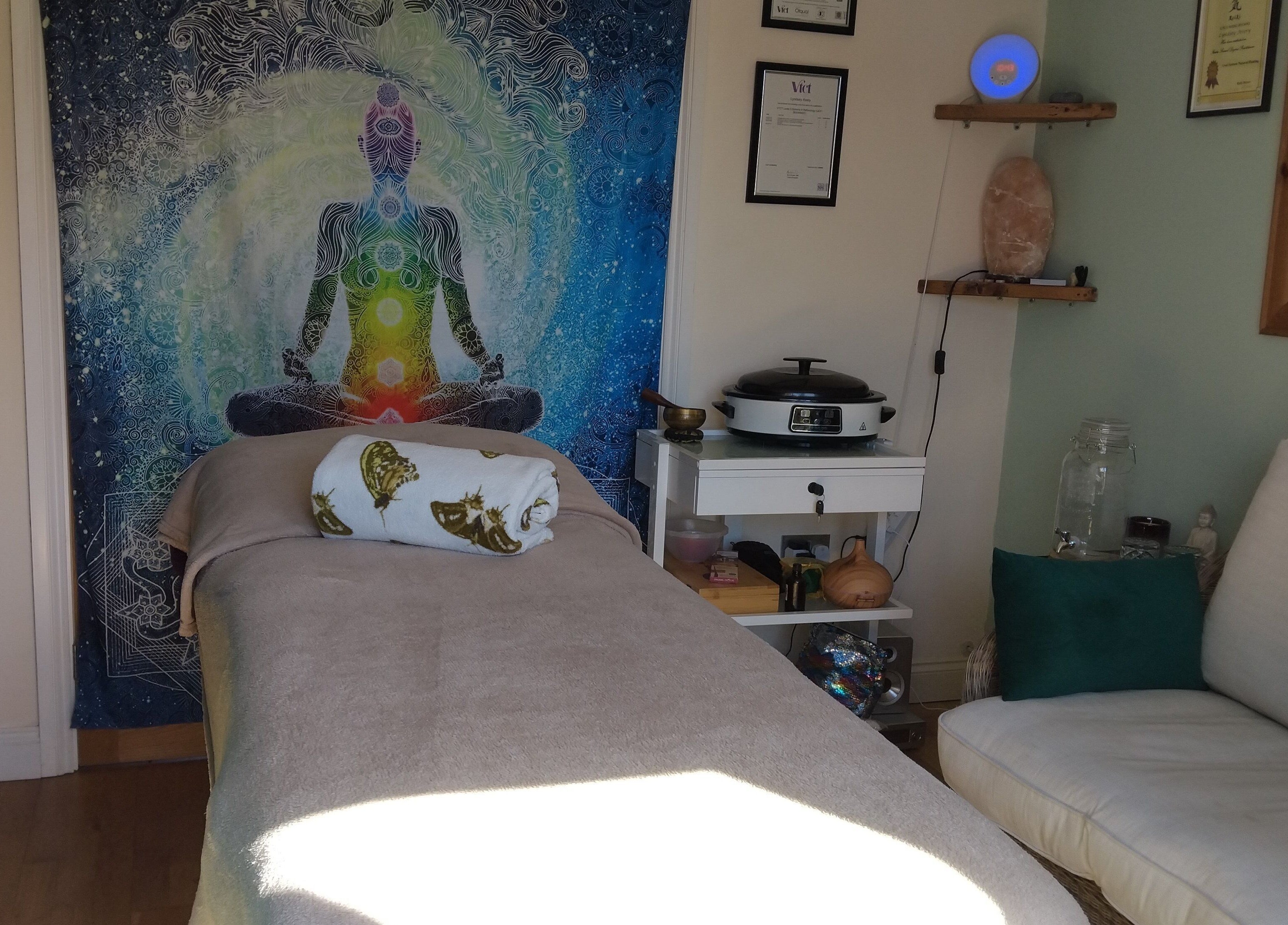 A serene therapy room at Bee Elevated Holistic Health in Holbury, England featuring a massage bed and chakra tapestry.