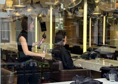 Виктория, парикмахер в ATHERTONCOX Salon, Лондон, Англия, обслуживает клиента на фоне современного интерьера.